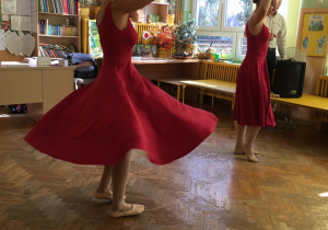 Baletnice tańczą, ubrane w czerwone suknie.