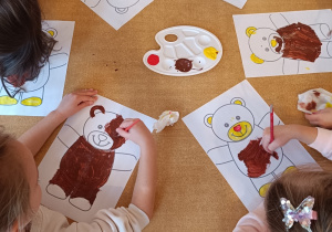 Dzieci malują przy stoliku farbami misie.