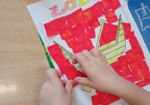 Dziecko przekleja kawałki czerwonej bibuły na swoją pracę - herb Łodzi.