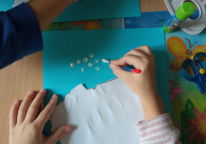 Dzieci malują patyczkami kosmetycznymi białe kropki na niebieskiej kartce.