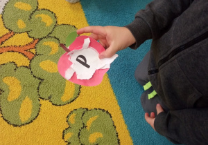 Dziecko pokazuje jaka literka kryła się w środku papierowego jabłuszka.