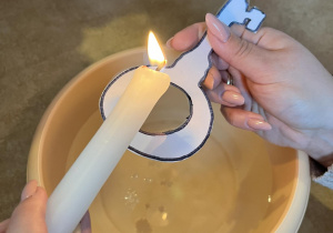 Nauczycielka trzyma papierowy, zalaminowany klucz przez który leje się wosk z zapalonej świeczki.