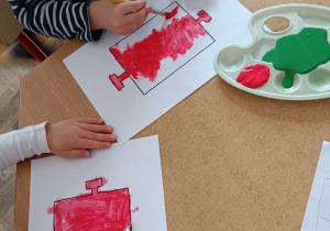 Dzieci przy stoliku malują farbami wagony.