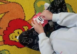 Dziecko rozdziera papierowe jabłuszko i odsłania literkę, która była ukryta w środku.