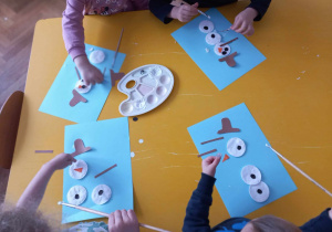Dzieci przyklejają elementy z jakich składa się bałwan do kartki.