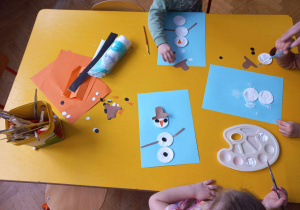 Dzieci przyklejają elementy z jakich składa się bałwan do kartki.