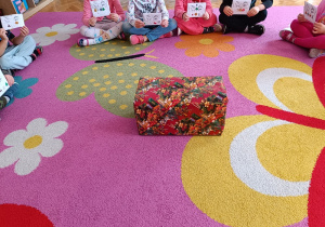 Dzieci siedzą na dywanie z listami do Mikołaja wokół magicznej skrzynki na listy.