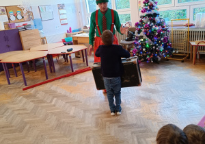 Chłopiec stoi z walizką w rękach i patrzy na mężczyznę przebranego za elfa.