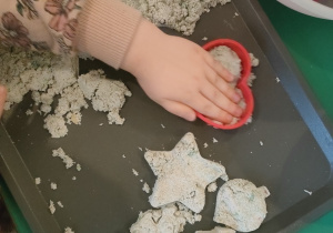 Dziewczynka robi serduszko w piasku kinetycznym za pomocą foremki do pierniczków.