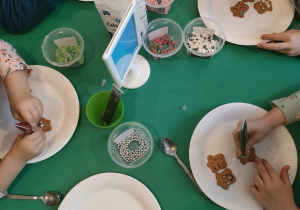 Dzieci przy stoliku dekorują pierniczki.
