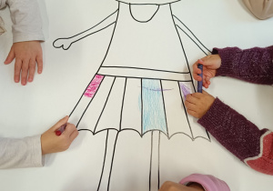 Dzieci kolorują postać dziewczynki na dużym kartonie.