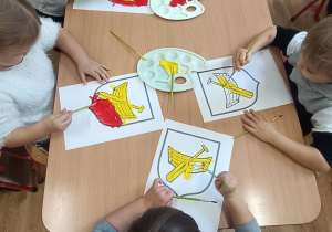Dzieci przy stoliku malują herb Łodzi farbami.