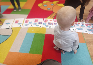 Chłopiec siedzi na dywanie i układa cyfry w odpowiedniej kolejności.