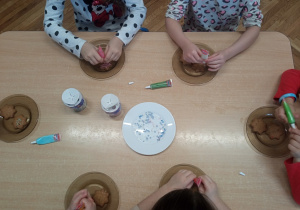 Dzieci dekorują cukrowymi pisakami korzenne ciasteczka.