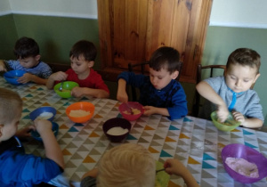 Dzieci siedzące przy pierwszym stole, mieszają w miseczkach.