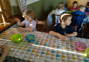 Dzieci siedzące przy drugim stole, mieszają w kolorowych miseczkach.