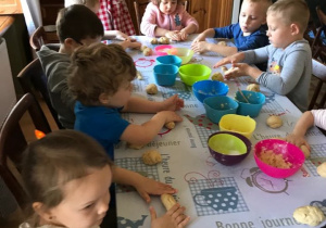 Dzieci siedzą przy stole, robią wałeczki z ciasta.