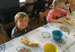 Dzieci siedzą przy stole, uśmiechają się, prezentują swoje warkocze z ciasta.