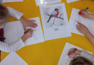 Dzieci przy stoliku kolorują według wzoru ptaki - gile.
