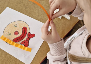Dziewczynka tworzy "włosy" dla klauna zaginając kolorowy pasek papieru.