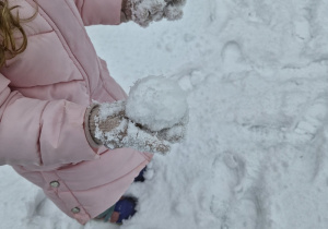 Dziewczynka w ogrodzie trzyma na ręce śnieżkę.