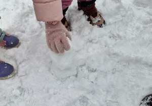 Dzieci lepią ze śniegu małego bałwanka.