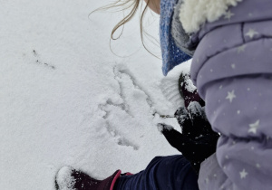 Dziewczynka rysuje serce patykiem na śniegu.