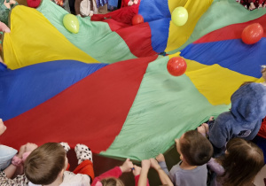 Dzieci trzymają chustę animacyjną podrzucając nią balony.