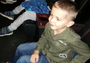 Chłopcy siedzą na miejscach w sali kinowej i uśmiechają się.
