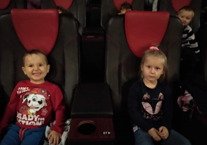 Dzieci siedzą na miejscach w sali kinowej i uśmiechają się