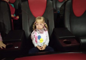 Dzieci siedzą na miejscach w sali kinowej i uśmiechają się