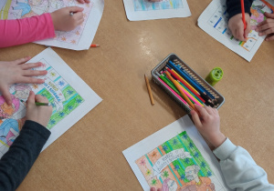 Dzieci kolorują kredkami tematyczne kolorowanki.