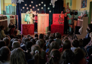 Dzieci oglądają przedstawienie teatralne. Na scenie aktorzy z lalkami teatralnymi.