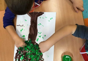 Dzieci malują paluszkami zamoczonymi farbą koronę drzewa.