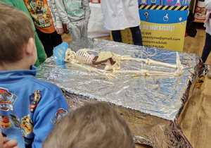 Dzieci stoją wokół stolika na którym leży szkielet człowieka.