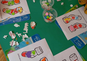 Dzieci przy stoliku przyklejają kolorowe naklejki na kontury skarpetek.