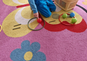 Chłopiec przelicza piłeczki znajdujące się w kolorowych obręczach.