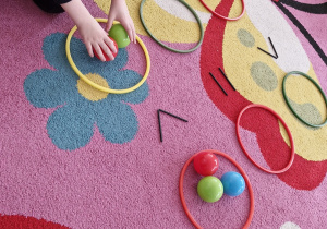 Dziecko układa kolorowe piłeczki po dwóch stronach symbolu mniejszości.