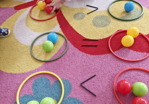 Dziecko układa kolorowe piłeczki po dwóch stronach symbolu większości.