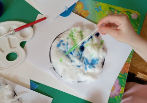 Dziewczynka maluje Ziemie wyklejoną watą z wykorzystaniem pipetki wypełnionej zieloną farbą.