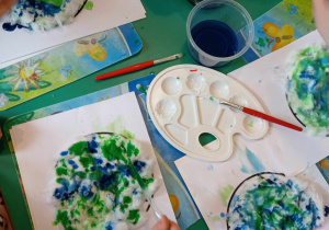 Dziewczynka maluje Ziemie wyklejoną watą z wykorzystaniem pipetki wypełnionej niebieską farbą.