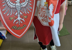 Chłopiec w stroju trzyma godło Polski na pokazie mody patriotycznej.