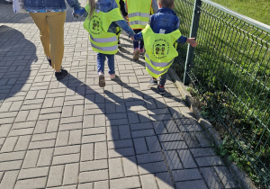 Dzieci w odblaskowych kamizelkach idą na miejsce zbiórki.