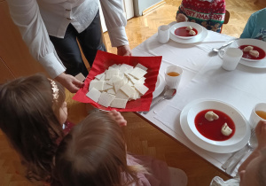 Dzieci biorą do rączek opłatek z talerza.