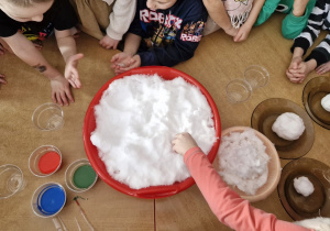 Na stoliku miska ze śniegiem, trzy śniegowe kule oraz różne barwniki.