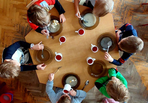 Dzieci siedzą przy stoliku i jedzą zupę.